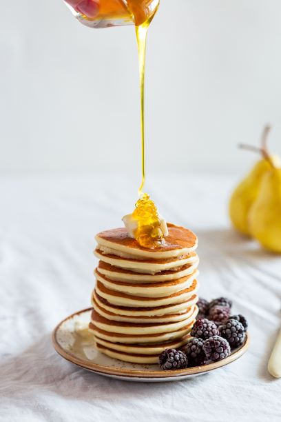 Stack of pancakes with berries on side of plate with honey