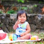 Toddler eating fresh fruits sitting on blanket outside