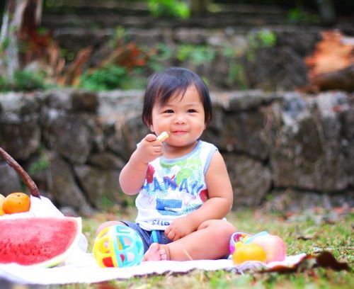 Toddler eating fresh fruits sitting on blanket outside