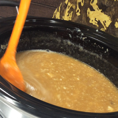 orange spoon stirs cooking pear butter in a slow cooker