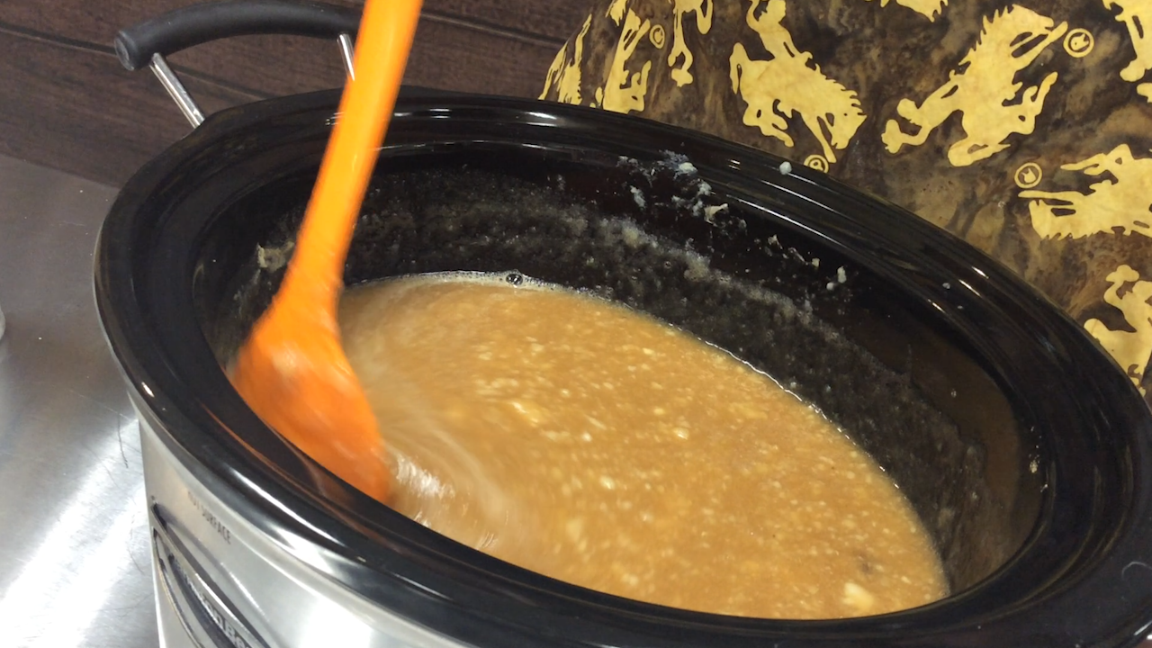 orange spoon stirs cooking pear butter in a slow cooker