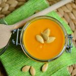 pumpkin soup with seeds on top. wooden spoon off to the side