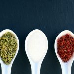 three spices in white spoons on blue background