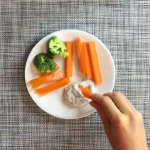 hand dipping carrot stick into dip