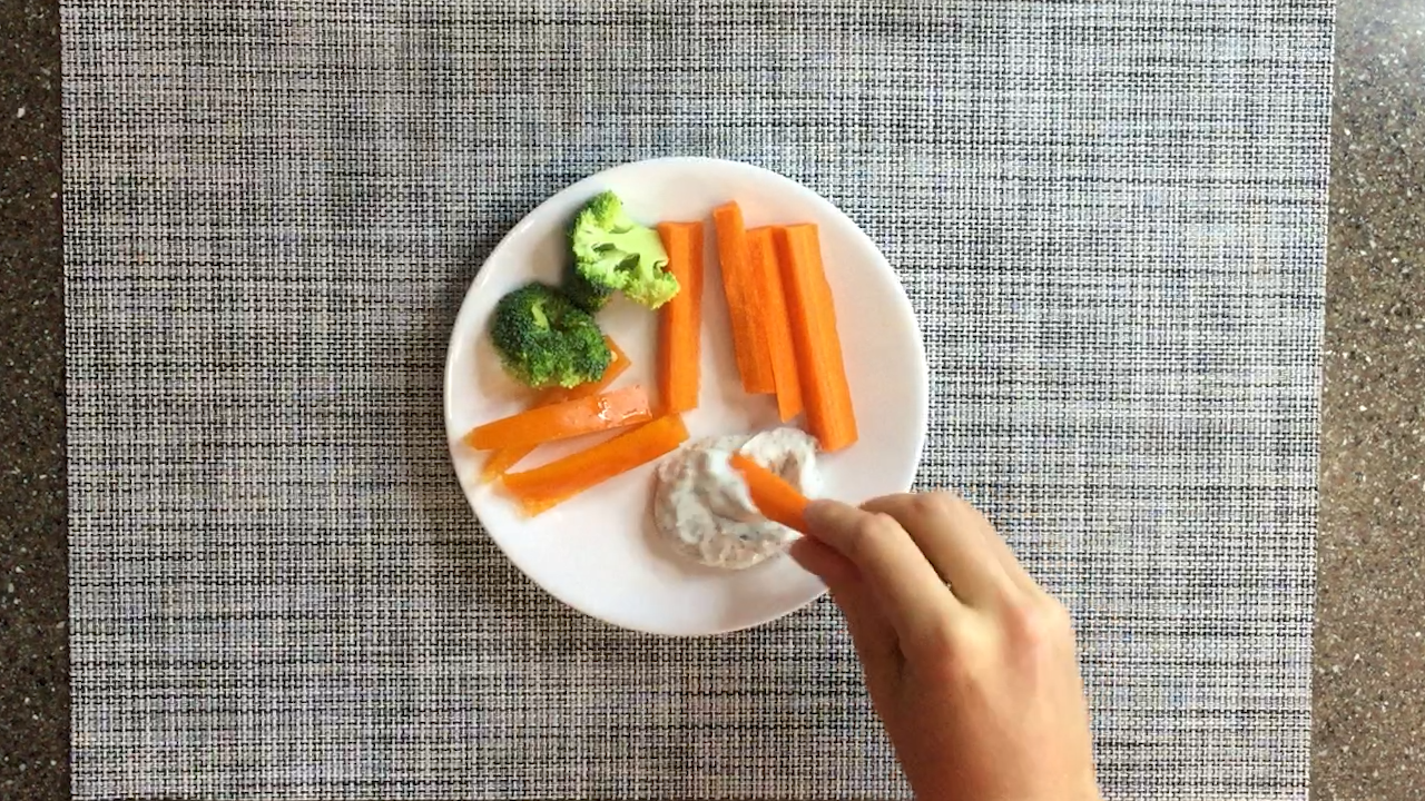 hand dipping carrot stick into dip