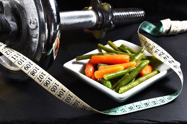 Bowl of vegetables with measuring tape and weights in background