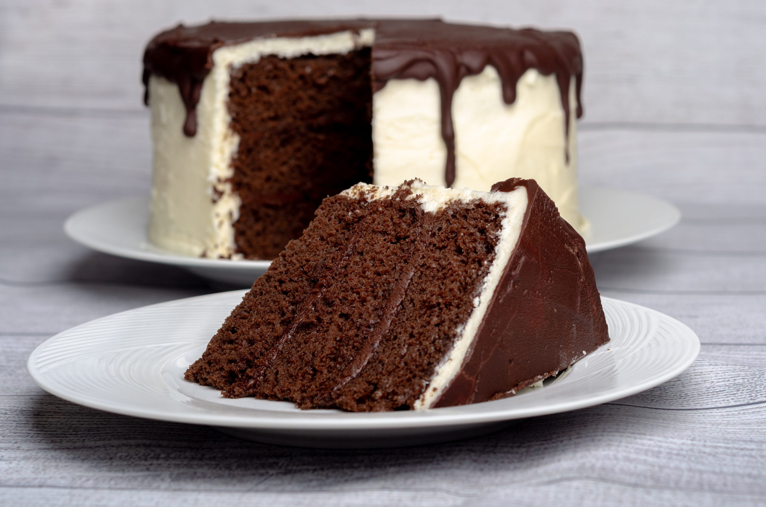 3 layered chocolate cake slice with chocolate frosting and rest of cake in background