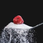 Spoon with sugar and one raspberry on top of sugar