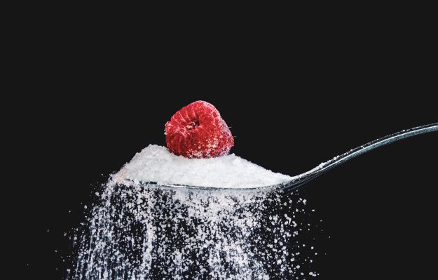 Spoon with sugar and one raspberry on top of sugar