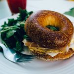 Breakfast bagel with greens on the side of the white plate