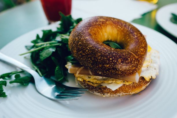 Breakfast bagel with greens on the side of the white plate