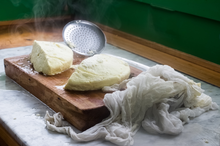 freshly made cheese on a cutting board near cheesecloth