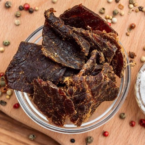 jerky sitting in a glass bowl with peppercorns and salt surrounding it