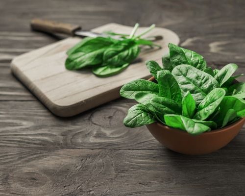 fresh spinach on a cutting board and in a bowl, knife next to cutting board