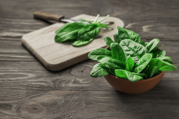 fresh spinach on a cutting board and in a bowl, knife next to cutting board