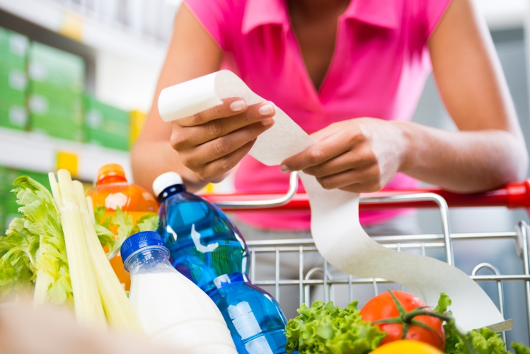 individual leaning on grocery cart with grocery receipt and cart full of groceries