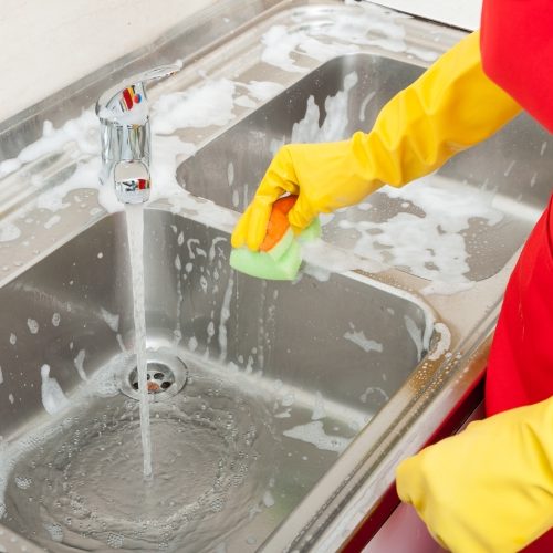 individual cleaning a sink with yellow rubber gloves and a sponge