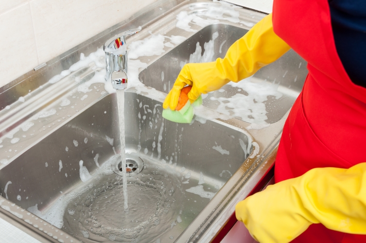 individual cleaning a sink with yellow rubber gloves and a sponge