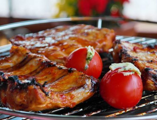 pork ribs on a grill with some fresh tomatoes
