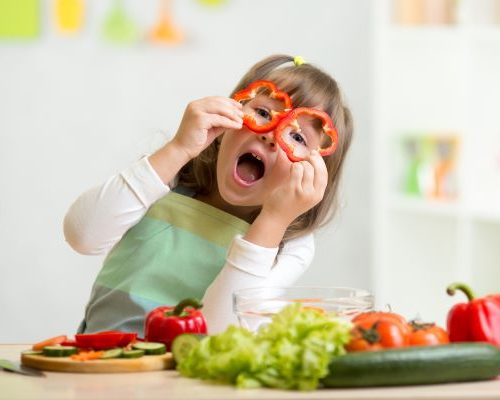 Child holding red pepper slices up to face like glasses