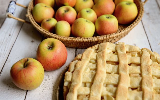 apple pie with fresh apples off to the upper left hand corner in a basket