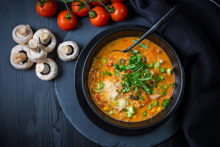 bowl of soup next to fresh mushrooms and tomatoes