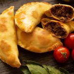 Empanadas filled with meat next to fresh tomatoes