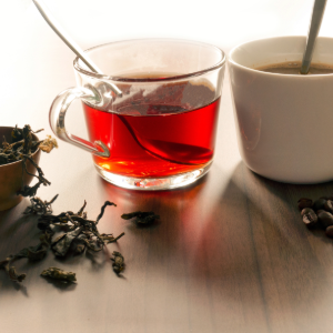 Glass cup of red tea and a white coffee mug with loose tea leaves and coffee beans on a wooden table.