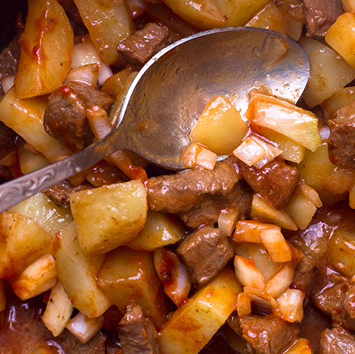 Close-up of a hearty wild game stew with potatoes, onions, and chunks of meat being stirred with a spoon.