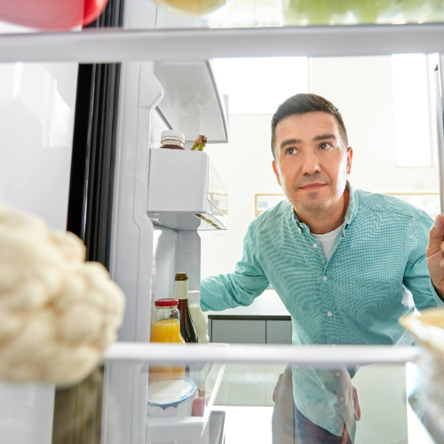 Man looking inside an open refrigerator while checking stored food items, illustrating evaluating food freshness and safe food storage at home.